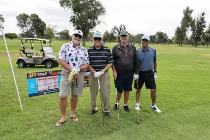 Four golfers with their clubs beside the 30th Golf Tournament sign