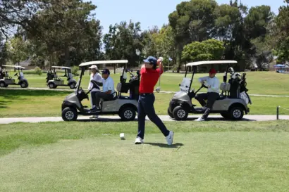 A golfer in a red shirt teeing off, with golf carts on the path behind