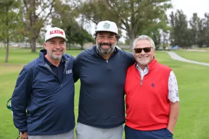 Three golfers smiling together on the course at the 30th Annual Benefit Golf Tournament